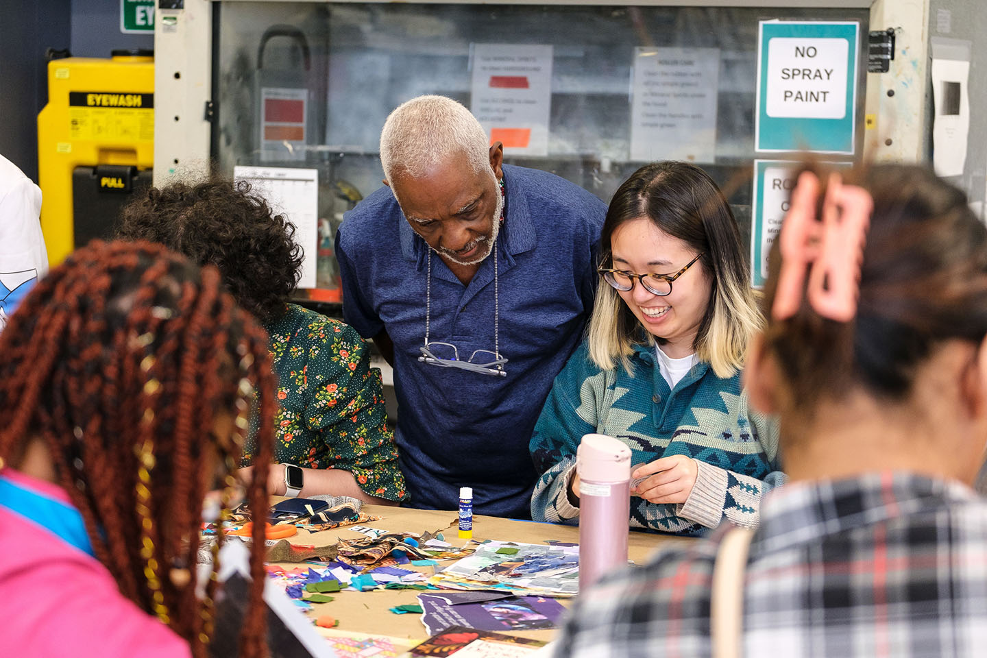 A group of people are gathered around a table covered with various art supplies and materials. They appear to be engaged in a collaborative art project.